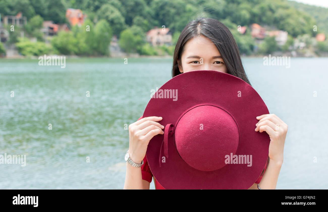 Mode femme holding hat standing in front of a lake Banque D'Images
