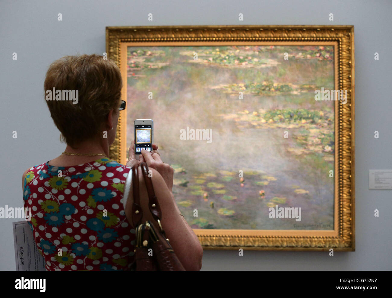 Un visiteur prend une photo sur son téléphone d'une œuvre de Claude Monet, Nympheas (Water Lilies), 1906, qui est estimée à 20-30 millions de livres sterling, lors d'une séance photo pour Sotheby's 250 millions de livres sterling Impressionist & Modern Art and Contemporary Art Summer Sales à New Bond Street, Londres. Banque D'Images