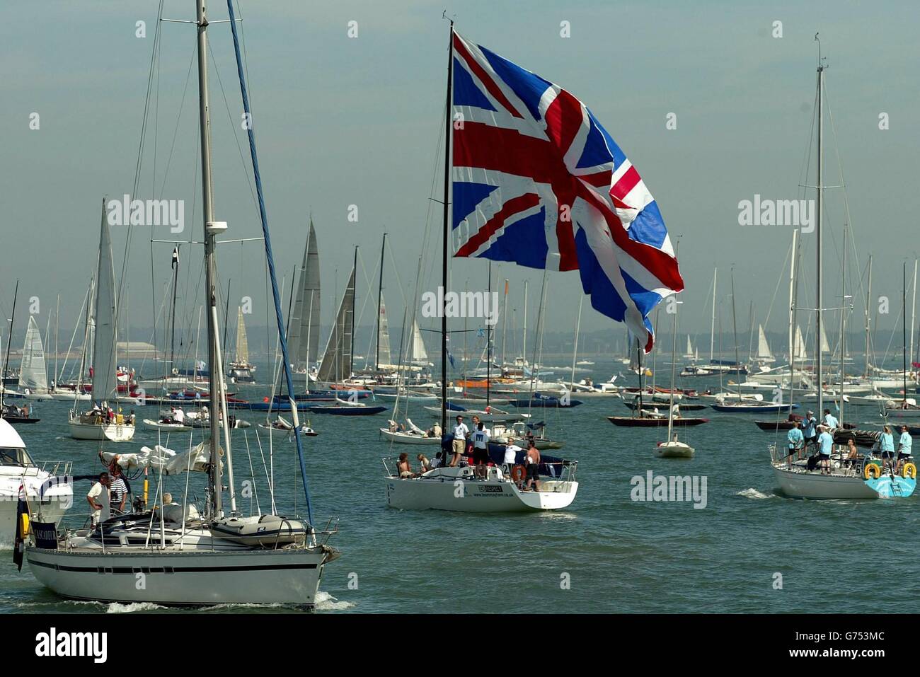 Un yacht vole un énorme jack d'Union alors qu'il sort de la médina sur l'île de Wight, où les conditions bénignes et le soleil élevé ne signifiait que peu de vent, retardant le début de la course le premier jour de la semaine des cowes de Skandia,la plus ancienne et la plus grande régate de voile au monde. Banque D'Images