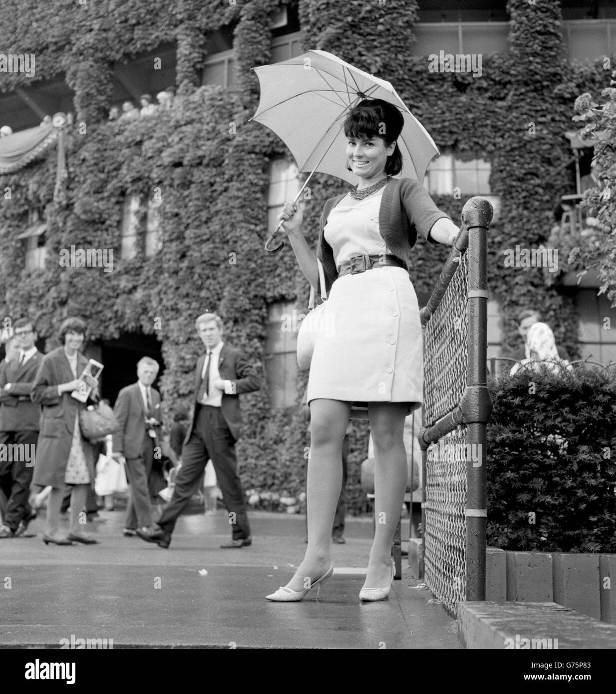 Eileen Sheridan, de Walton-on-Thames, une ancienne Miss Grande-Bretagne et Miss Royaume-Uni, se protège de la pluie sous un parapluie aux championnats de tennis de Wimbledon. Banque D'Images