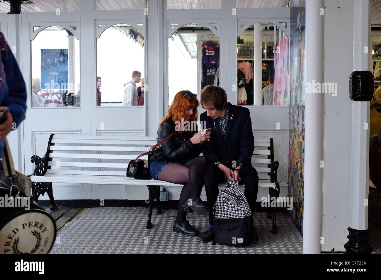 Un jeune couple assis sur un banc blanc de sms. Banque D'Images