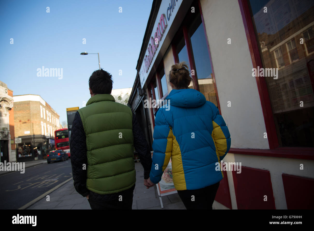 Dans l'homme veste puffer vert, la femme en bleu et jaune veste puffer de derrière, Stoke Newington, Londres. Banque D'Images