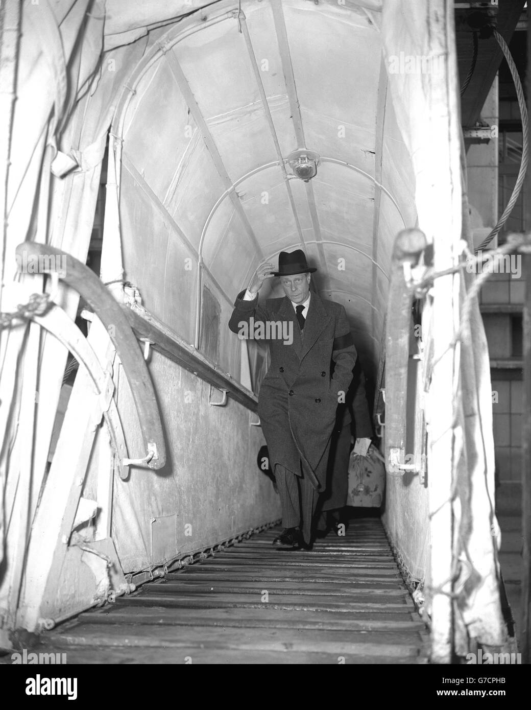 Le duc de Windsor, portant un chapeau trilby noir et une bande noire sur le bras gauche de son pardessus gris, se promène sur le gangway du paquebot Cunard Queen Elizabeth à Southampton.Le duc revient aux États-Unis pour rejoindre la duchesse après avoir assisté aux funérailles de sa mère, la reine Marie. Banque D'Images