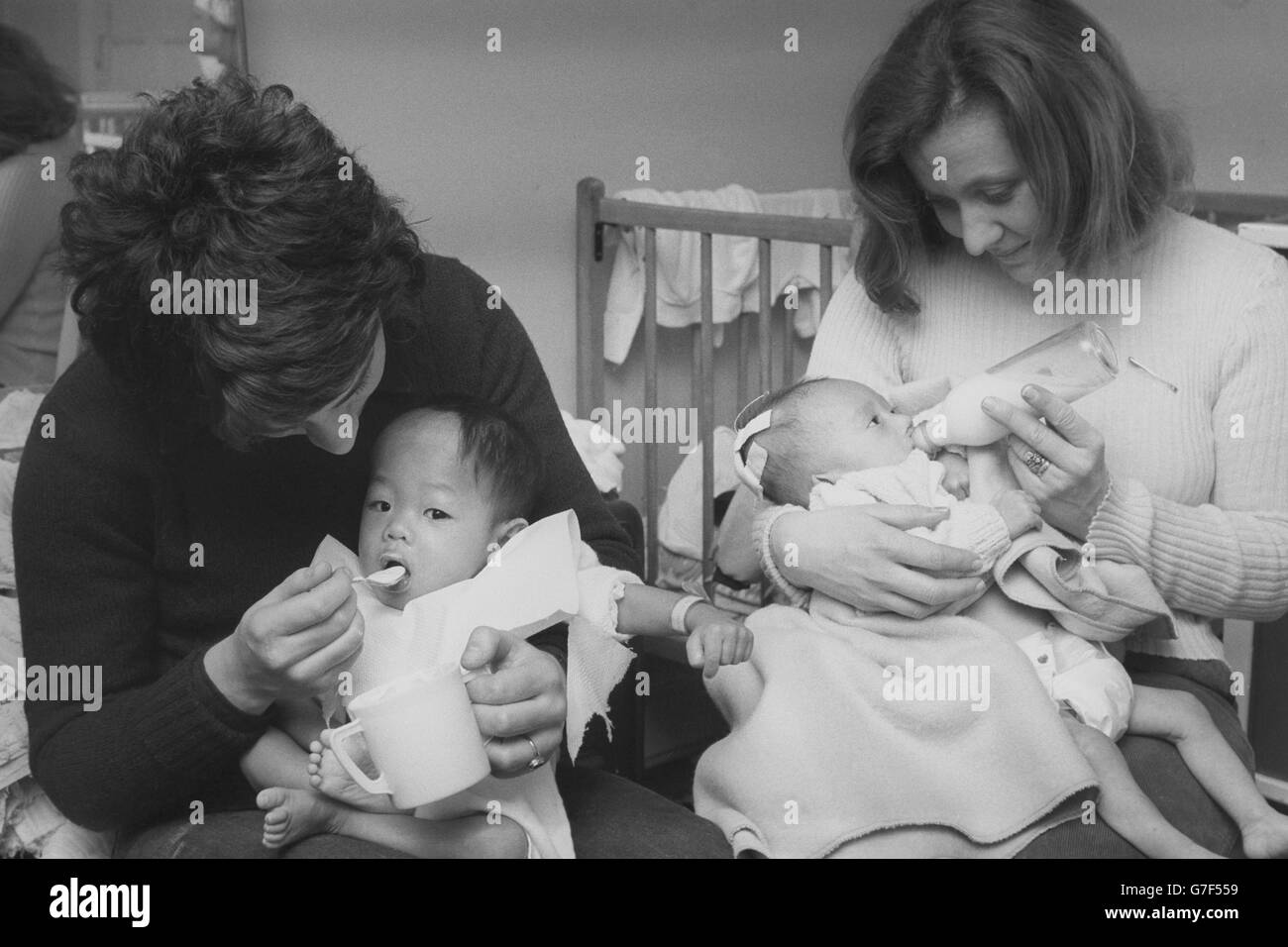 Deux jeunes bébés sont nourris au centre Ockenden Venture de Haslemere, Surrey, par les assistants Ross Tennyson (l) et Diana Dollery. Les bébés faisaient partie d'un groupe d'enfants qui sont arrivés du Vietnam la nuit dernière. Banque D'Images