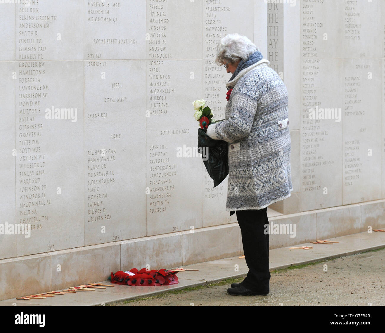 Un membre du public dépose des fleurs sur un mur portant le nom du personnel des forces armées déchus lors des commémorations du jour de l'armistice à l'Arboretum du Mémorial national d'Alrewas, dans le Staffordshire. Banque D'Images