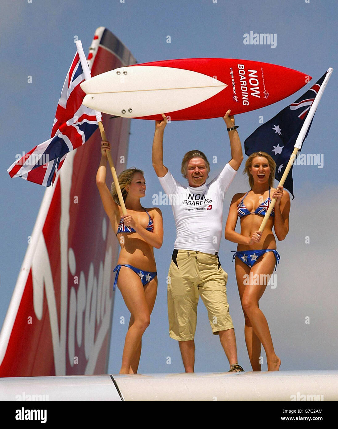 Sir Richard Branson se tient sur l'aile de son nouvel avion, avec deux modèles portant des drapeaux du Royaume-Uni et de l'Australie, après son atterrissage à l'aéroport international de Sydney pour marquer le lancement du vol inaugural de Virgin Atlantic vers l'Australie depuis le Royaume-Uni via Hong Kong. Banque D'Images