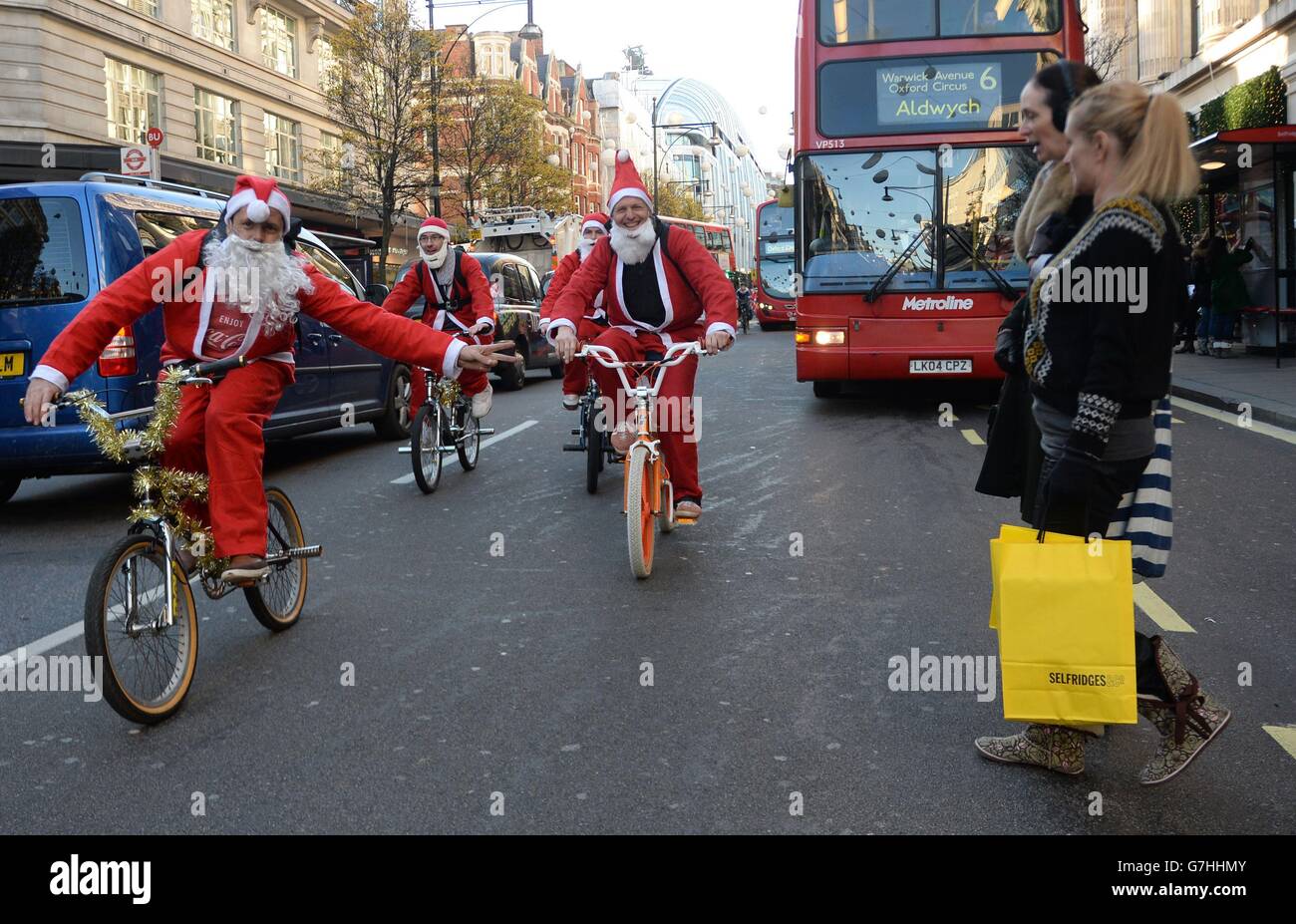 Les acheteurs regardent des gens habillés comme le Père Noël monter en vélo à Oxford Street, Londres. Banque D'Images