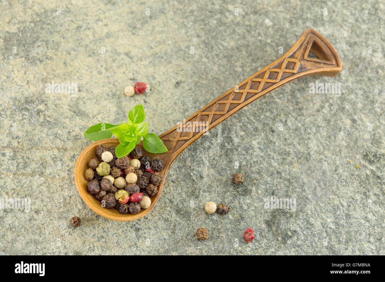 Grains d'épices poivre dans une cuillère en bois sur une table en pierre Banque D'Images