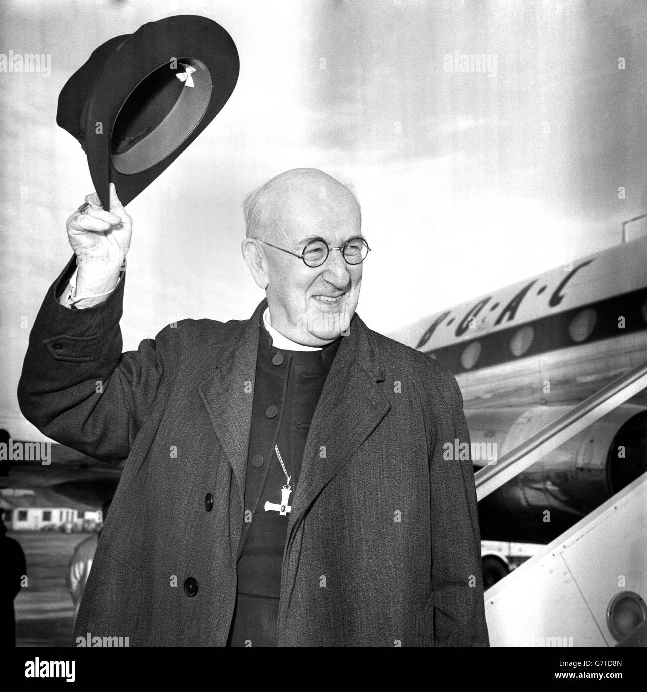 Souriez et une large vague d'adieu du chapeau du Dr. Geoffrey Fisher, l'Archevêque de Canterbury, à l'aéroport de Londres à propos de monter dans un avion pour Beyrouth à la première étape d'un pèlerinage à la Terre Sainte, Istanbul et Rome, où il doit rencontrer le Pape. Banque D'Images