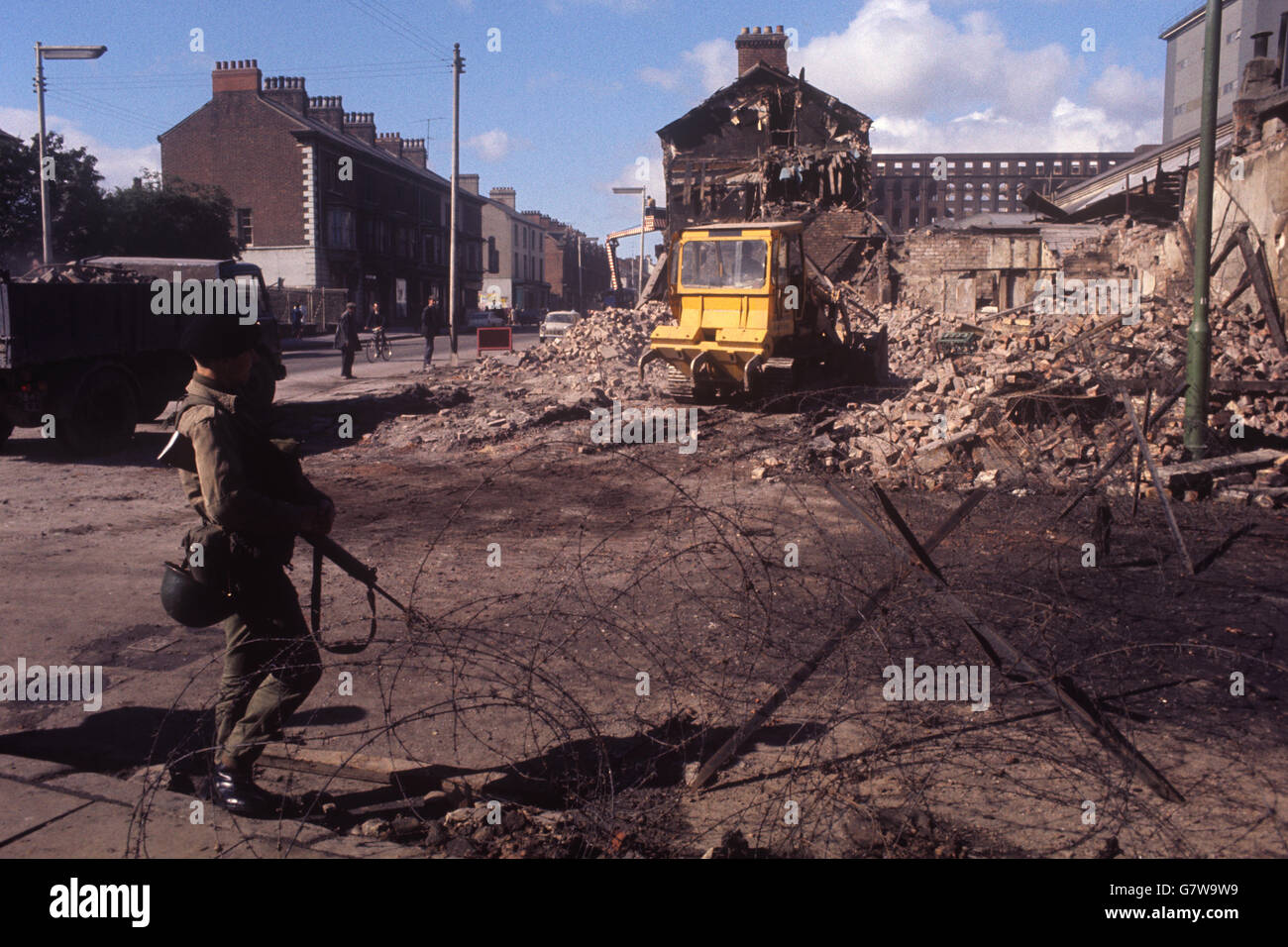 Un soldat à une barrière de barbelés dans un contexte de dévastation à Falls Road, Belfast. Banque D'Images