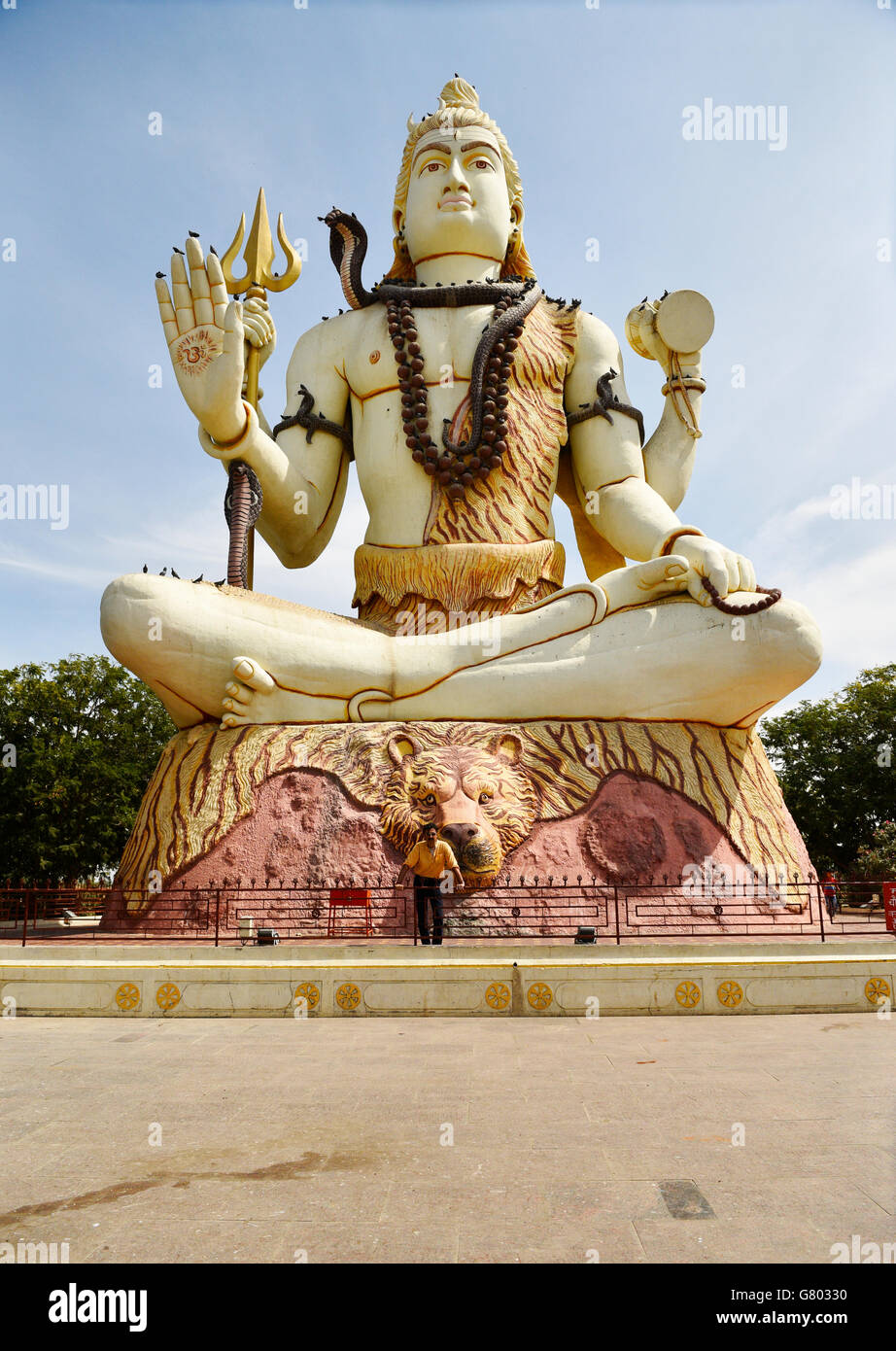 Un homme debout au bas de l'immense statue du dieu Shiva qui bénit bienvenue à tous les pèlerins visitant Nageshwar temple dans le Gujarat. Banque D'Images