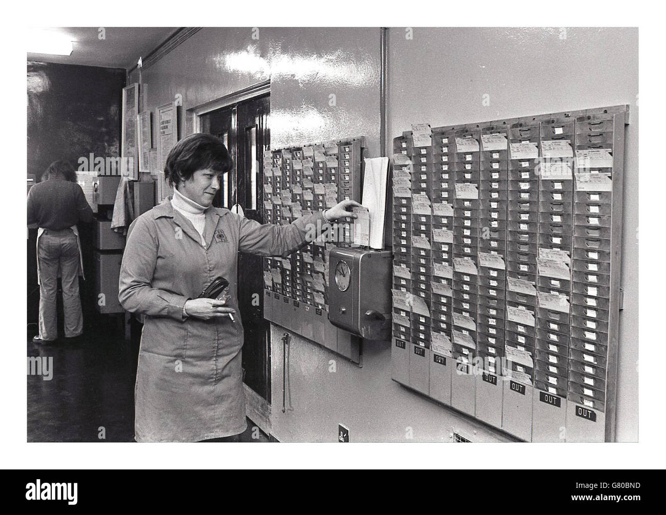 Années 1970, historique, l'image montre une femme de pointage au travail en mettant sa carte d'employé dans l'horloge ou l'horloge de pointage. Banque D'Images