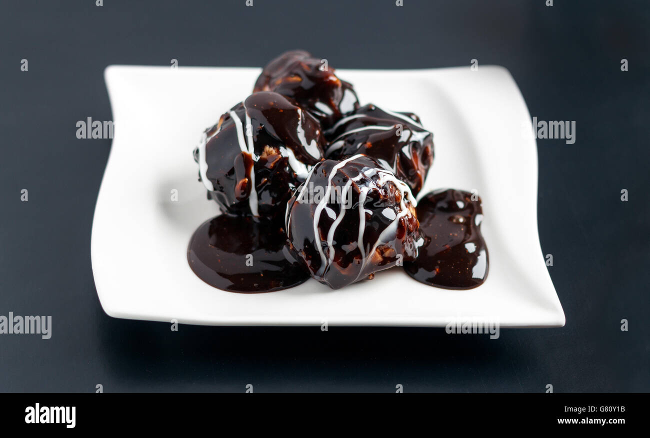 Profiterole pièces sur une plaque blanche recouverte de crème au chocolat et sucre en poudre Banque D'Images