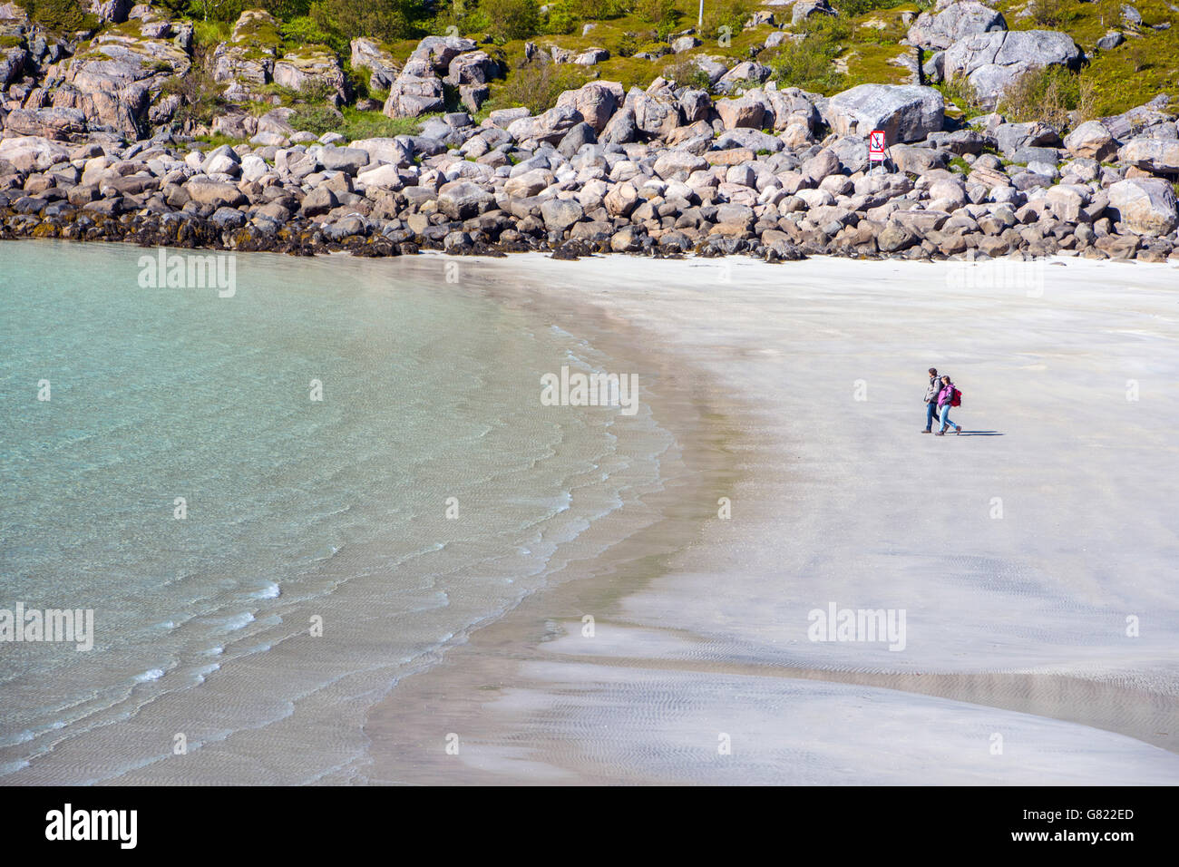 Deux personnes sur plage déserte, l'aigue-marine bleu de la mer avec les îles Lofoten, Norvège arctique boulders Banque D'Images