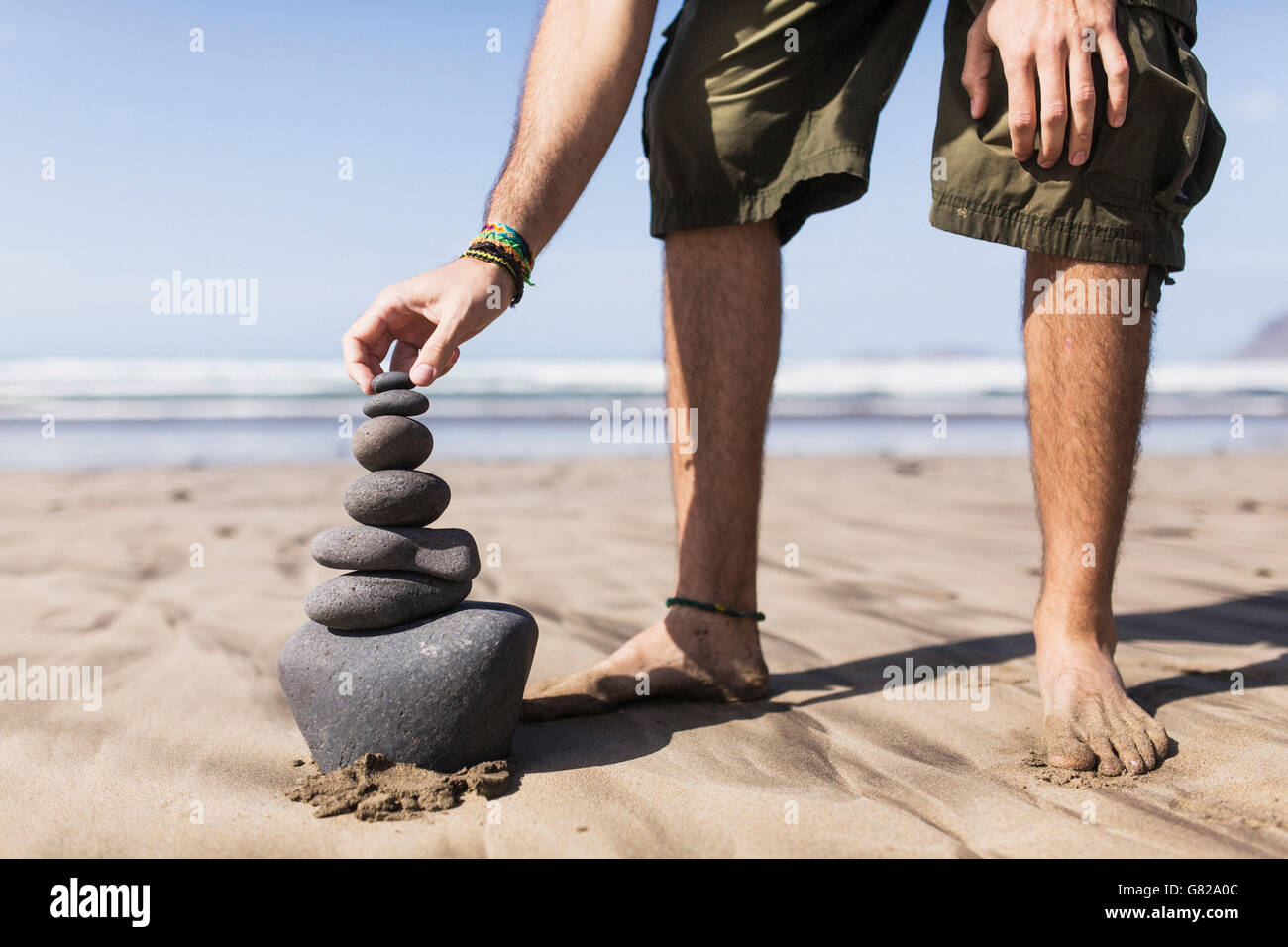 La section de l'équilibrage de l'homme faible pile de pierres sur beach Banque D'Images
