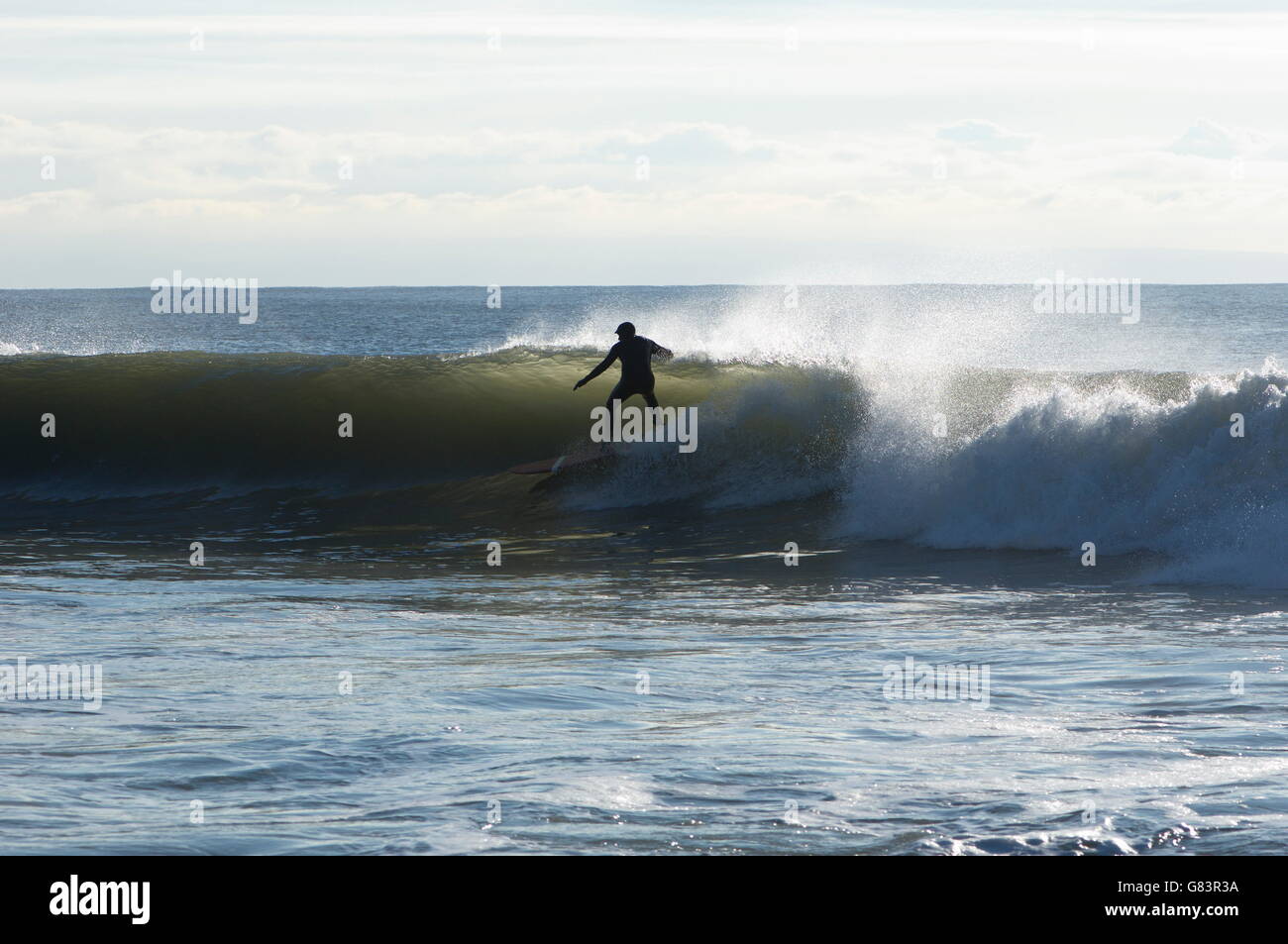 Surfer en silhouette par la lumière à travers l'onde courses la déferlante sur un point break au Pays de Galles. Le surf est un sport populaire pour les touristes. Banque D'Images