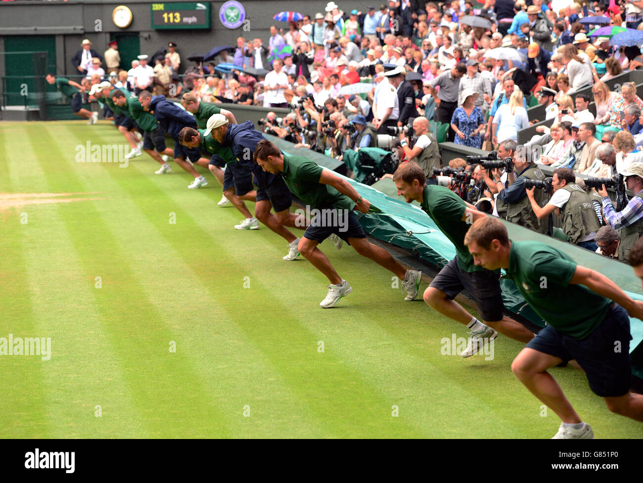 Le personnel de terrain couvre le terrain pendant que les arrêts de pluie jouent pendant la finale des hommes célibataires le treize jour des championnats de Wimbledon au All England Lawn tennis and Croquet Club, Wimbledon. Banque D'Images