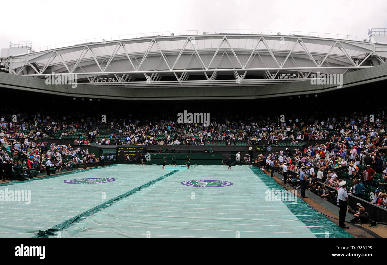 Le personnel de terrain couvre le terrain pendant que les arrêts de pluie jouent pendant la finale des hommes célibataires le treize jour des championnats de Wimbledon au All England Lawn tennis and Croquet Club, Wimbledon. Banque D'Images