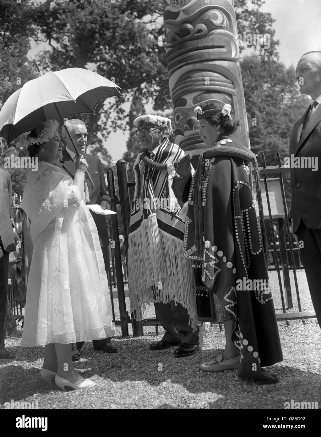 La reine Elizabeth la reine mère, qui était députrice de la reine Elizabeth II, s'entretient avec le chef Mungo Martin et sa petite-fille, Helen Hunt, après avoir reçu le totem de 100 pieds, un cadeau de la Colombie-Britannique, dans le Grand parc de Windsor. Le chef Mungo Martin, des Indiens Kwakiutl, une tribu située sur l'île de Vancouver, a sculpté l'ornementation élaborée sur le poteau de 12 tonnes. Le cadeau de totem à la reine Elizabeth II marque le centenaire de la Colombie-Britannique. Banque D'Images