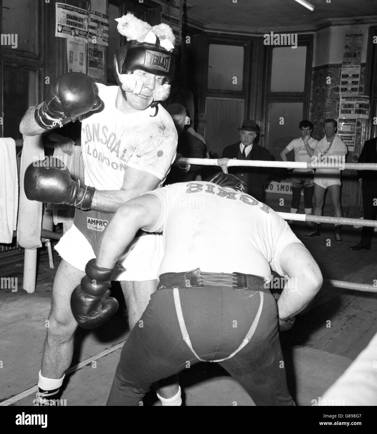 Le champion britannique de poids lourd Henry Cooper parte avec Giorgio Masteghin au gymnase Thomas a'Beckett dans Old Kent Road. Il porte une protection spéciale sur son visage pour éviter les coupures, tandis que le rembourrage sur le dessus de sa tête rend le protège-tête plus adapté. Banque D'Images