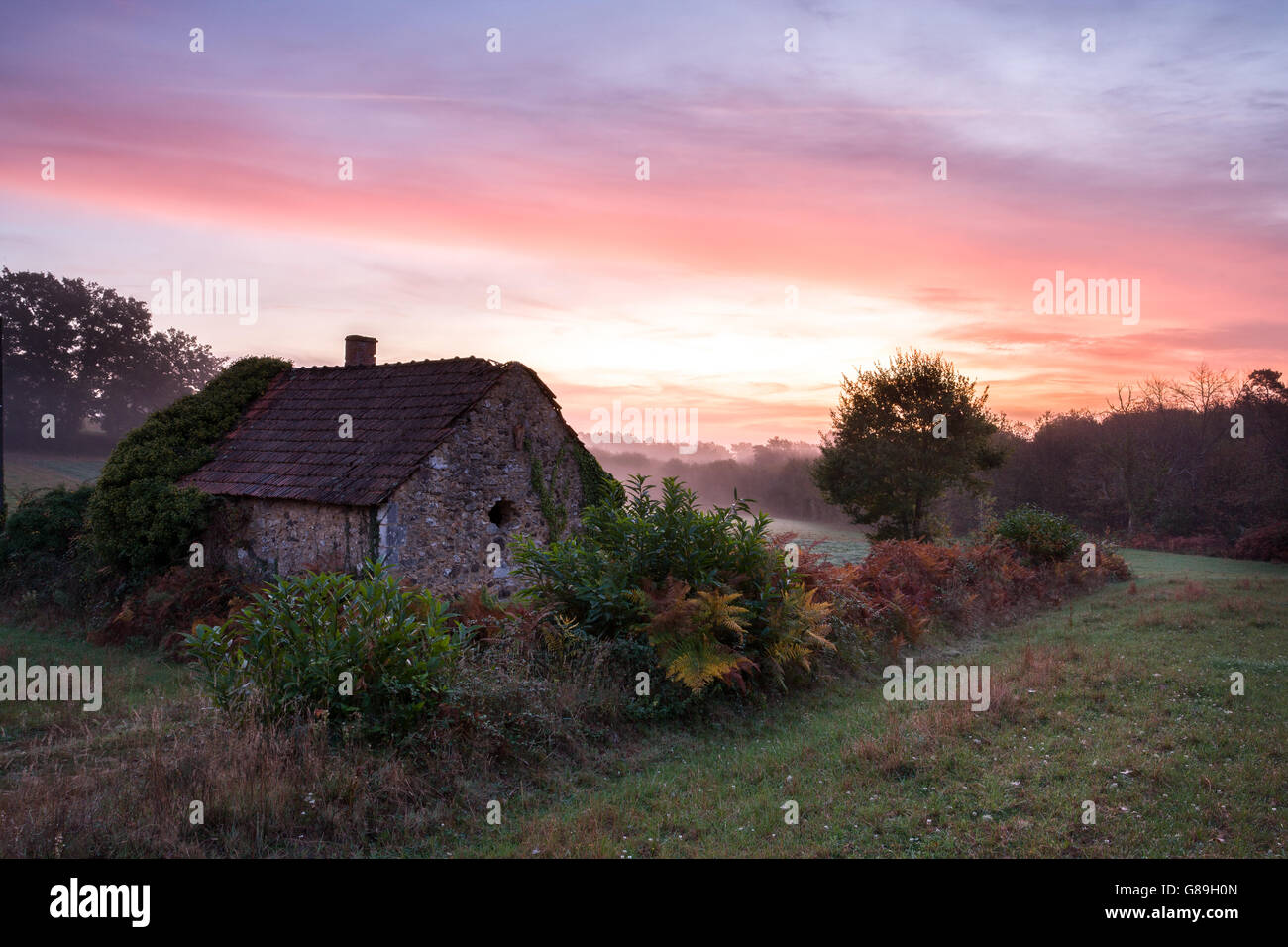 Cottage abandonné au lever du soleil avec un ciel coloré et de la brume Banque D'Images
