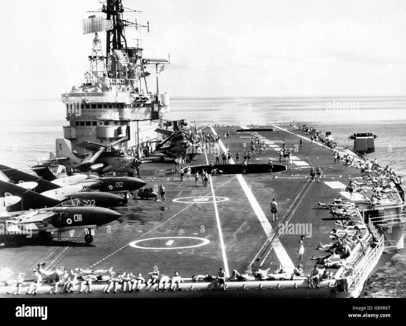 Les marins se prélassent au soleil à bord du porte-avions HMS Ark Royal dans le canal du Mozambique, tandis que les avions Gannet et Sea Vixen sont aéroportés.Les autres avions sont prêts sur le pont pour la sortie suivante. Banque D'Images