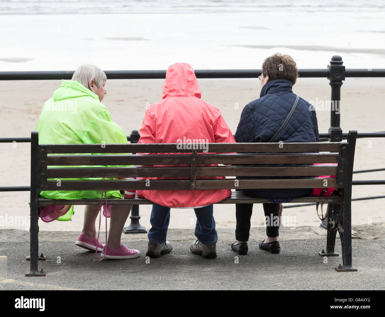 Vue arrière de trois femmes d'âge mûr assis sur banc avec vue sur plage un jour froid, gris en Angleterre. UK Banque D'Images