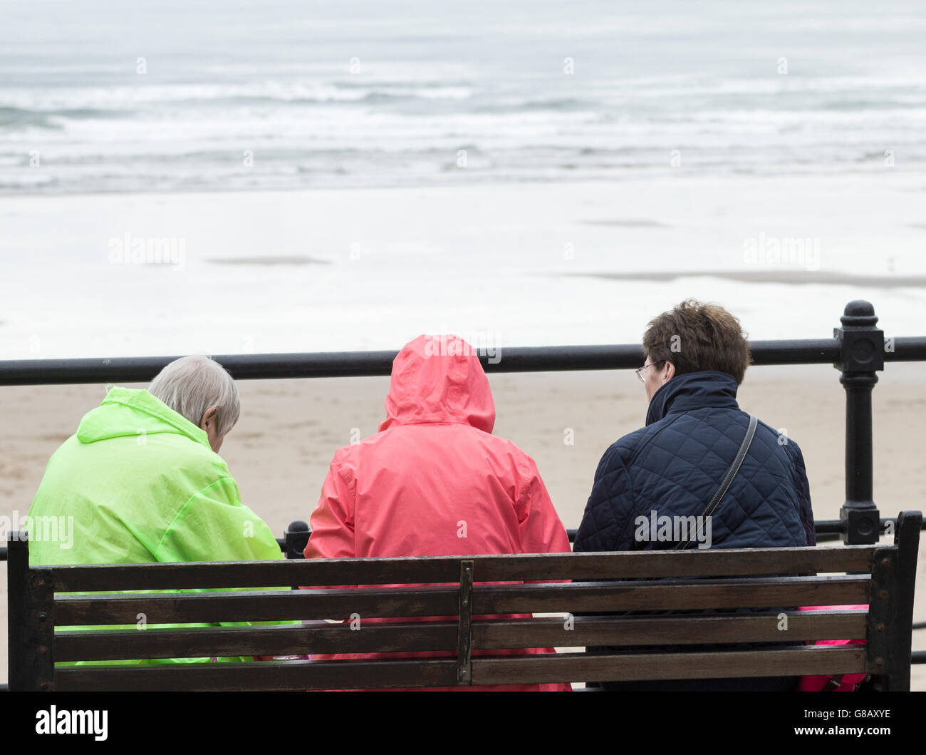 Vue arrière de trois femmes d'âge mûr assis sur banc avec vue sur plage un jour froid, gris en Angleterre. UK Banque D'Images