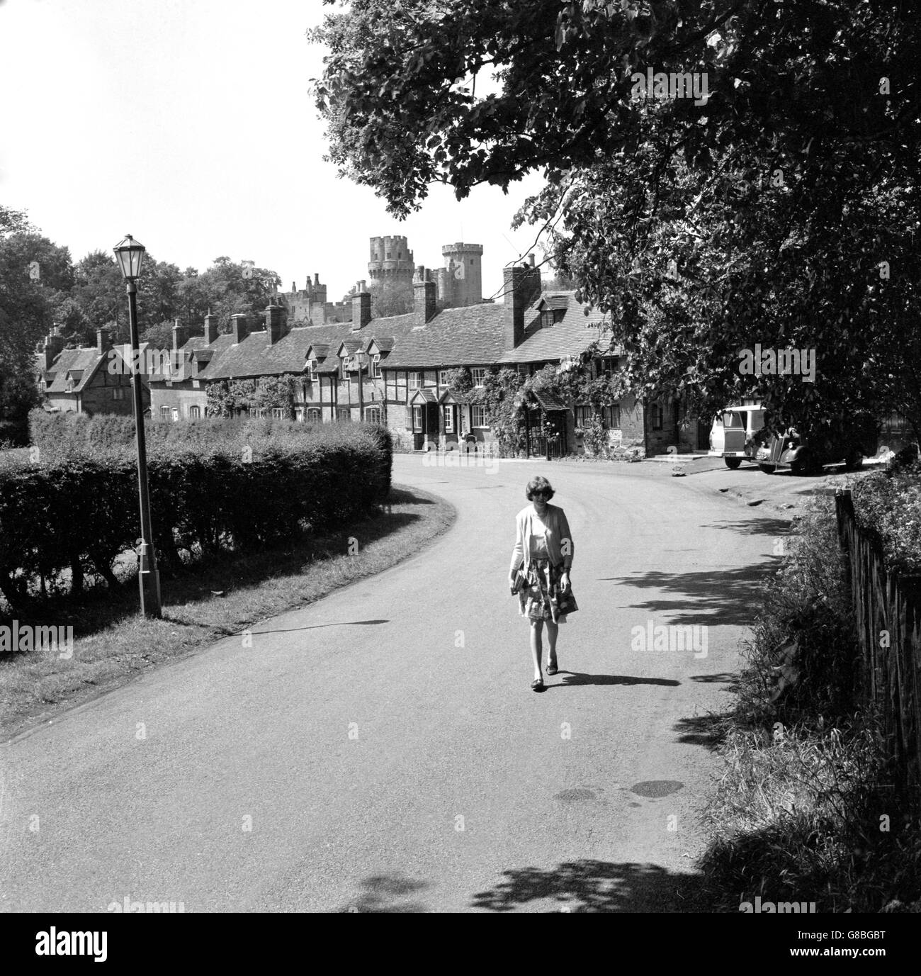 Les tours et les remparts du château de Warwick dominent cette rangée de cottages à pans de bois à Warwick. La tour de gauche est la tour César de 160 pieds de haut, achevée en 1356. À droite se trouve la Tour Guy's de 93 pieds de haut, construite en 1394. Banque D'Images