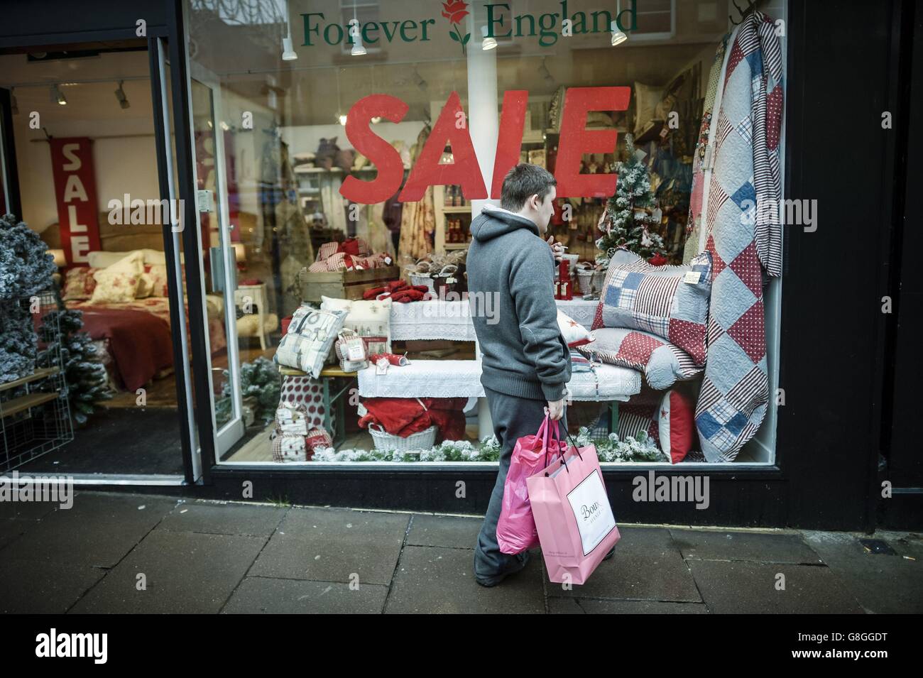 Un homme tient des sacs à l'extérieur d'une boutique avec une affiche de vente à Bath, alors que les acheteurs de panique et les chasseurs de bonnes affaires devraient inonder les magasins le jour le plus chargé du calendrier de Noël aujourd'hui, avec des boutiques de grande rue qui badent les prix pour tenter d'attirer les consommateurs dans les allées. Banque D'Images