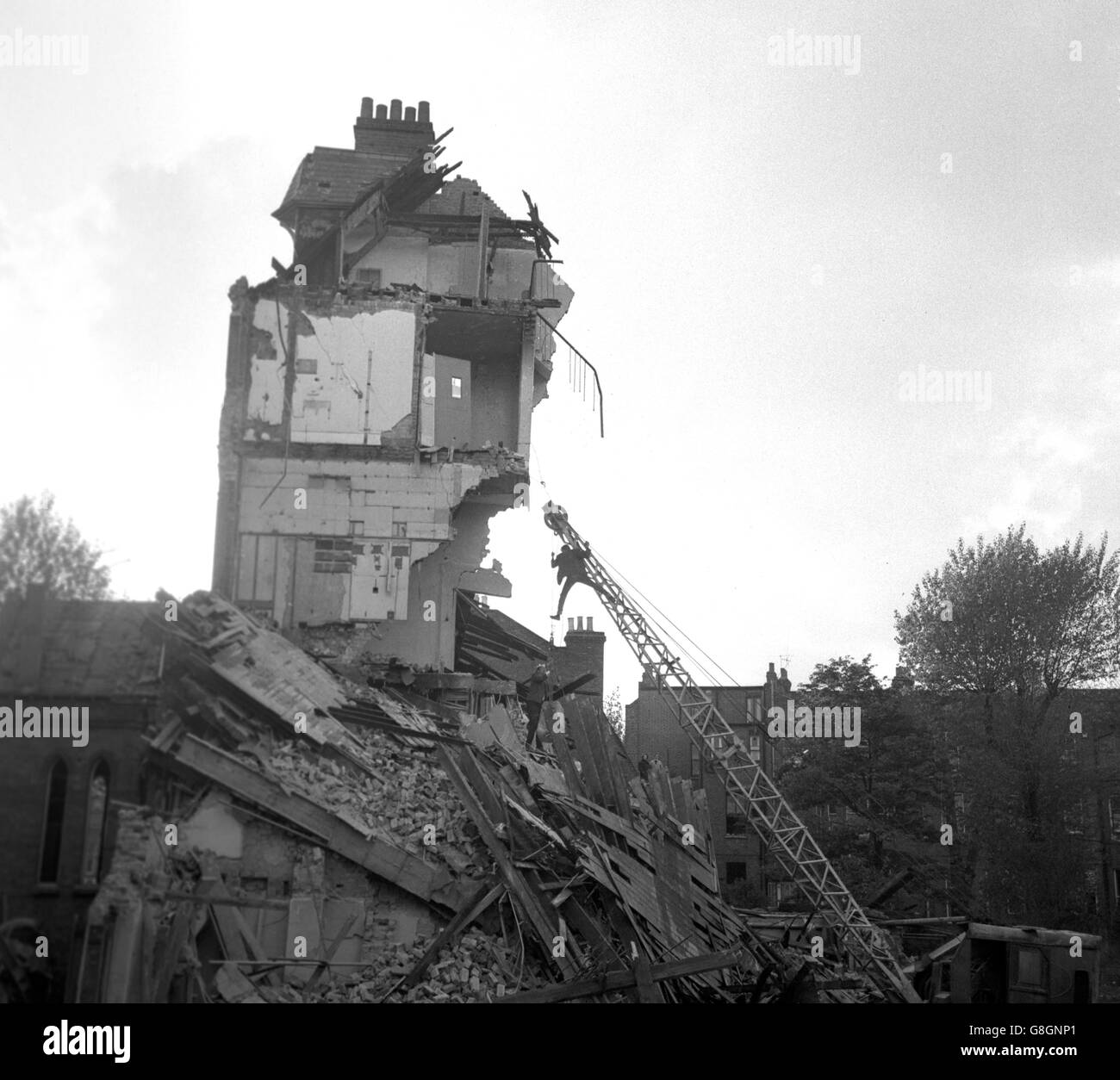 Il y avait un grand danger que l'imposante pièce centrale de ce bâtiment en cours de démolition tombe dans le mauvais sens, dans Shirland Road, Maida Vale, Deux ouvriers de démolition audacieux, Harry Shailey et Cyril Bere, ont donc monté le brancard de la grue et fixé un pont-beur pour pouvoir le faire descendre comme prévu. La raison du danger soudain était qu'un incendie a éclaté dans l'ancien bâtiment, l'ancien département de transcription de la British Broadcasting Corporation, au cours des progrès précédents de la tâche de démolition de la dernière semaine, ce qui a entraîné la tour à pencher sur le mauvais chemin. Dans cette photo, les hommes sont vus Banque D'Images