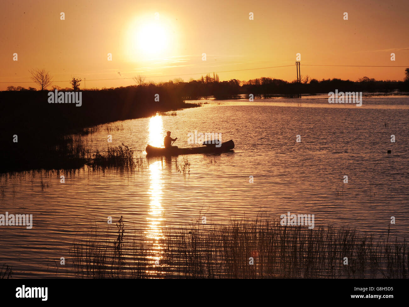 Le soleil se lève tandis qu'un homme et son chien font une excursion en canoë sur de grandes zones de terres agricoles couvertes d'eau de crue de la rivière Wharfe, entre Bolton Percy et Tadcaster. Banque D'Images