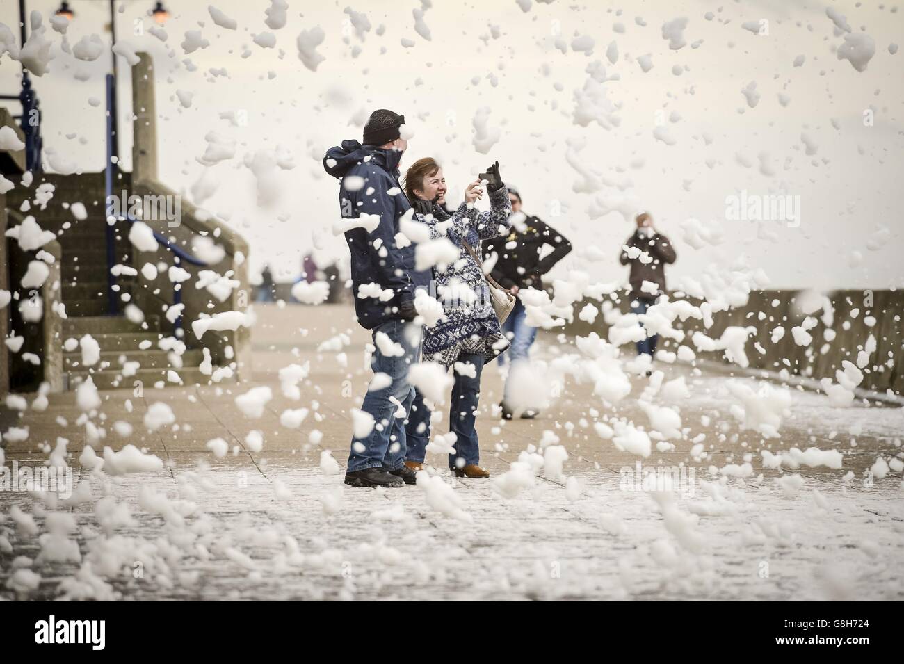 Les gens traversent les jets des vagues qui se brisent près du mur du port de Porthcawl, au sud du pays de Galles, alors que Storm Desmond frappe le Royaume-Uni. Banque D'Images