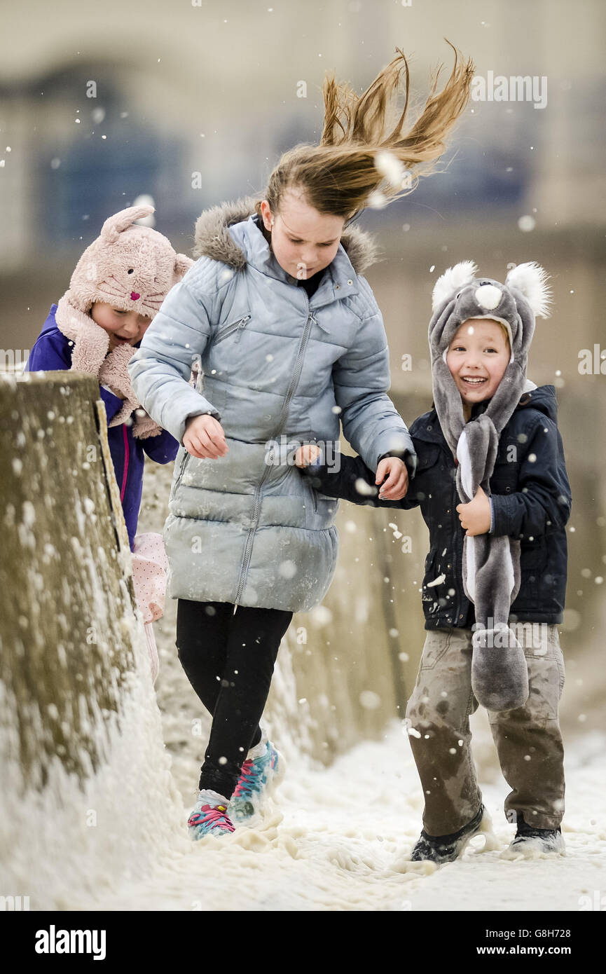 Les frères et sœurs Lauren (au centre), 11 ans, Geneviève, six ans, et Tobi, quatre ans, sont asperés par des vagues qui s'écrasant près du mur du port de Porthcawl, au sud du pays de Galles, alors que Storm Desmond frappe le Royaume-Uni. Banque D'Images