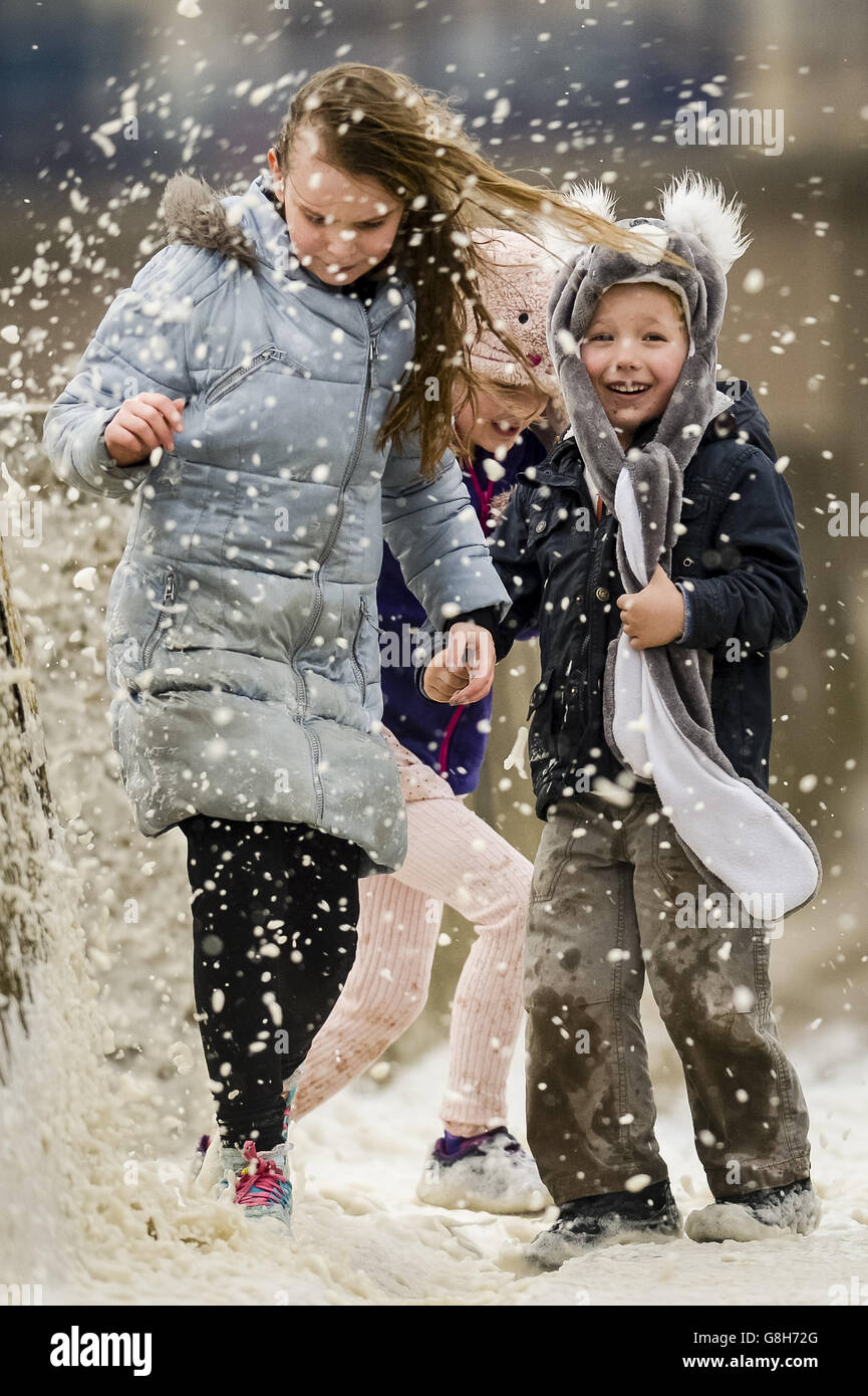 Les frères et sœurs Lauren (à gauche), 11 ans, Geneviève, six ans, et Tobi, quatre ans, sont asperés par des vagues qui s'écrasant près du mur du port de Porthcawl, au sud du pays de Galles, alors que Storm Desmond frappe le Royaume-Uni. Banque D'Images