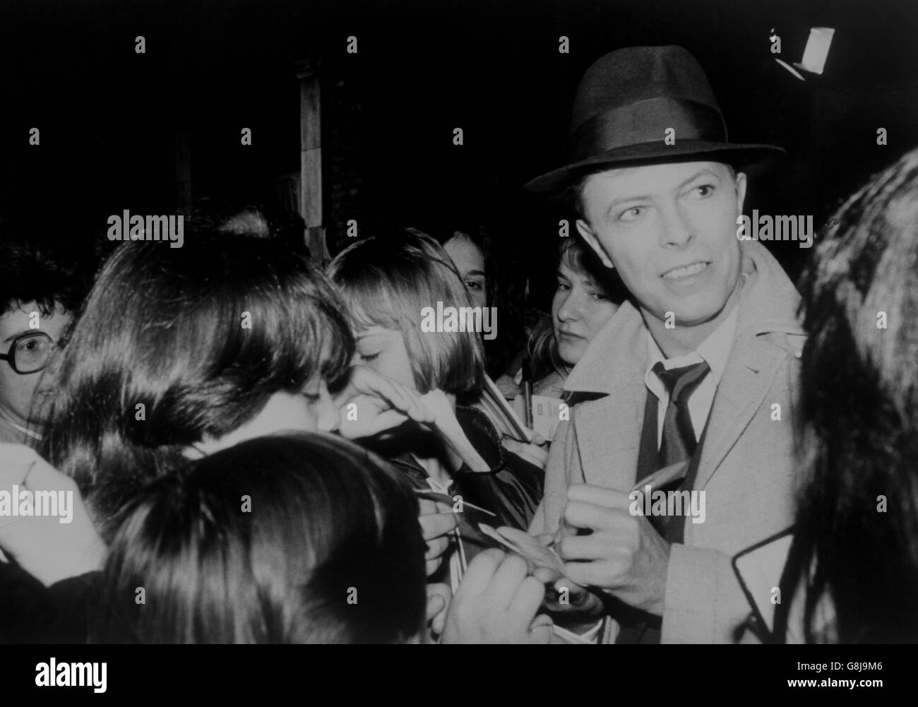 David Bowie signe des autographes pour des filles de bureau surprise qui se sont heurtées à la pop star trilby dans une rue de Londres. Il faisait une pause dans le tournage de son nouveau film « Absolute Beginners » dans un quartier fermé de Londres. Banque D'Images