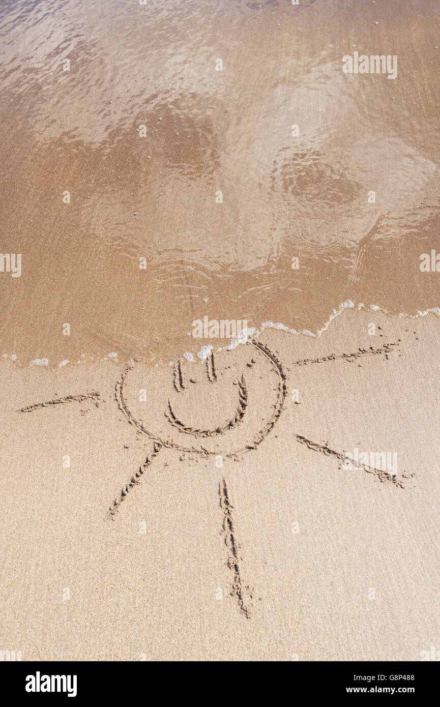 Smiley soleil de face dessin sur une plage. UK Banque D'Images