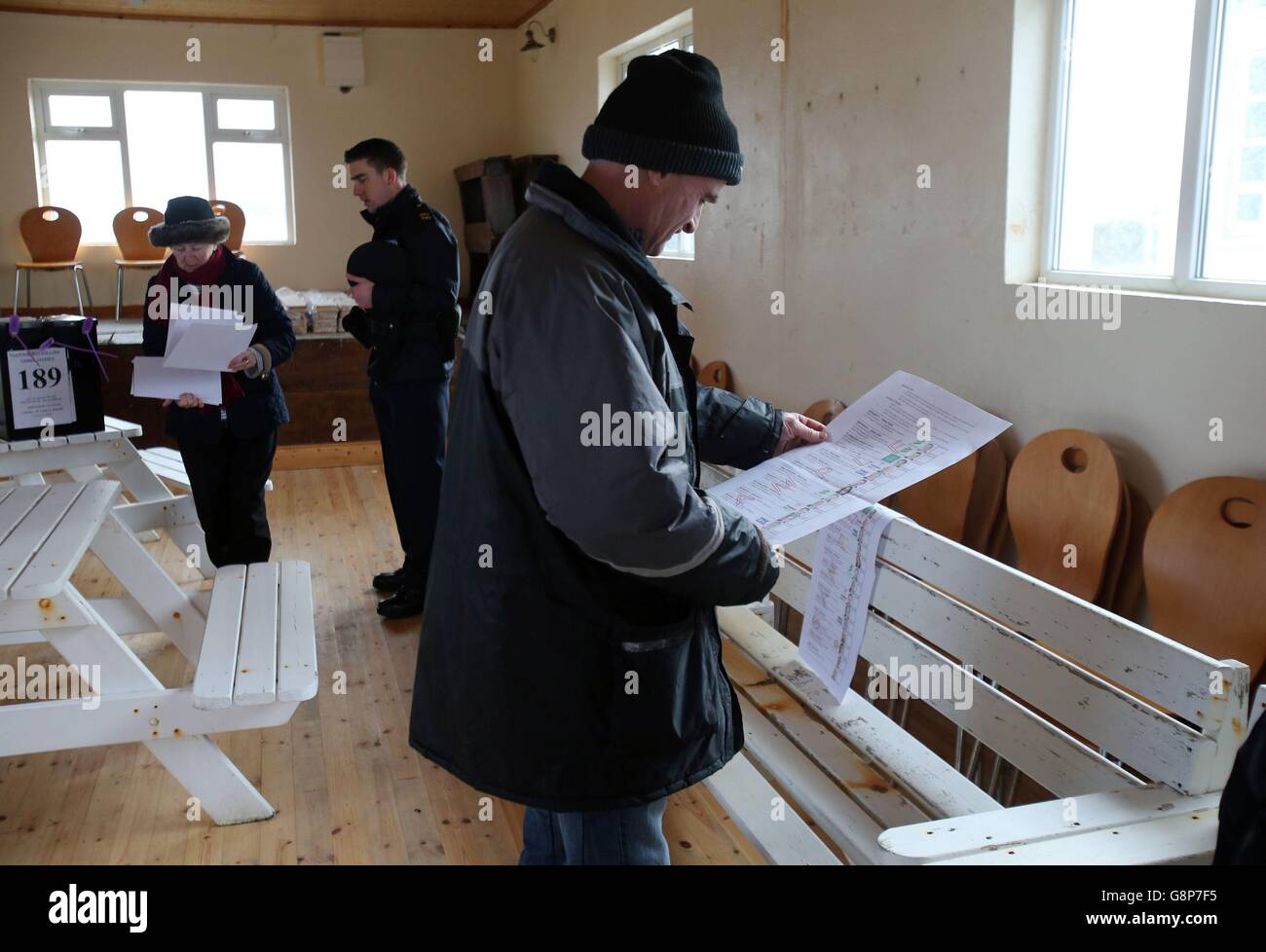 Peadar O'Brien, un résident local, examine un bulletin de vote type à titre d'officier présidant Carmel McBride et de sergent de Garde Paul McGee ouvre un bureau de vote sur l'île d'Inishbofin. Les électeurs de l'île éloignée, au large des côtes de Donegal, seront parmi les premiers à voter aux élections générales en Irlande, un jour avant le reste du pays. Banque D'Images