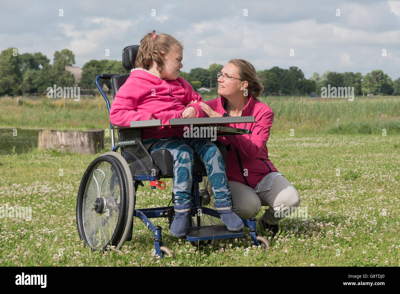 Une personne handicapée dans un fauteuil roulant à l'extérieur de détente avec l'aide d'un travailleur de volontaires Banque D'Images