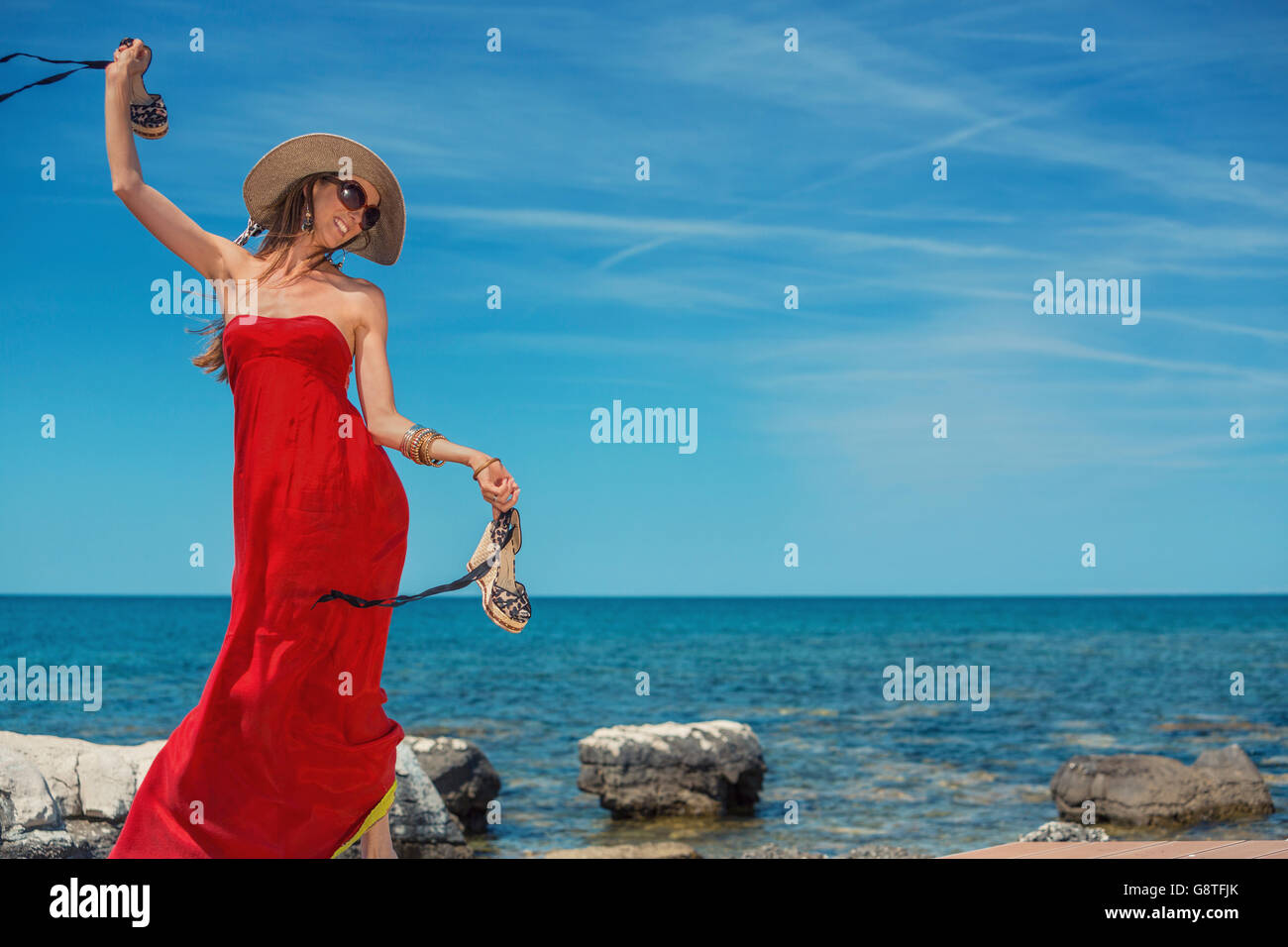 Belle femme en robe d'été rouge danser au bord de la mer Banque D'Images