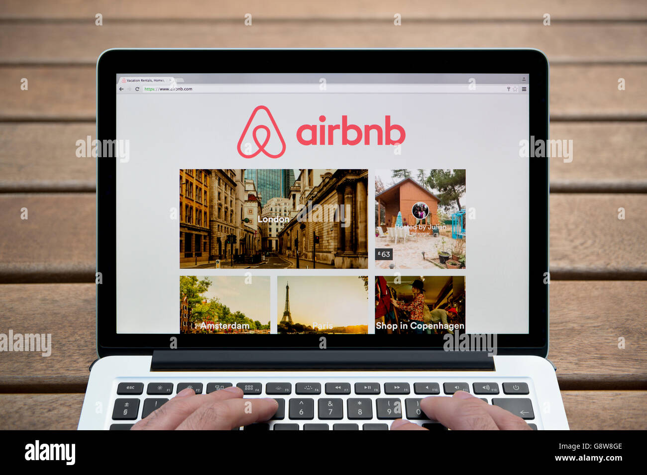 Le site Airbnb sur un MacBook contre un banc en bois fond de plein air y compris les doigts d'un homme (usage éditorial uniquement). Banque D'Images