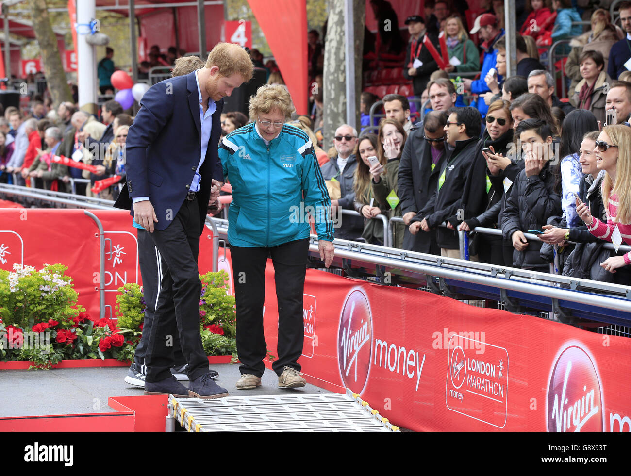 Le Prince Harry escorte la veuve du fondateur du London Marathon John Disley du podium après qu'elle est tombée pendant le Virgin Money London Marathon de 2016. Banque D'Images