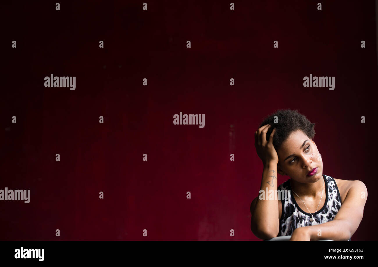 La beauté en déréliction : la photographie de mode d'une jeune afro-caraïbes femme fille seule dans une chambre aux murs rouge portant les vêtements de style, de remise en forme à chaud, sensuel et moody Banque D'Images