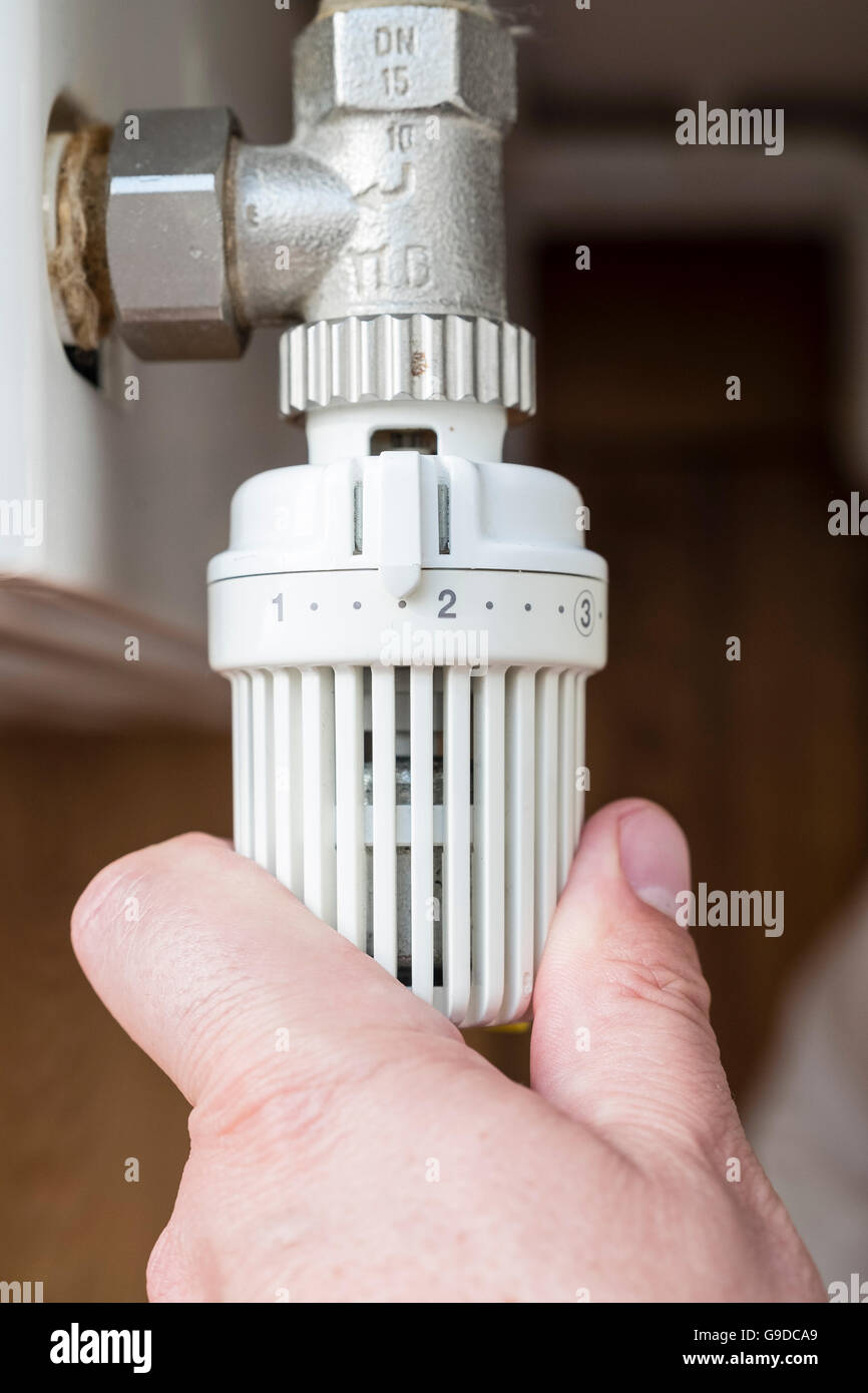 L'homme le fait de baisser le thermostat sur radiateur chauffage central au  gaz pour économiser de l'énergie Photo Stock - Alamy
