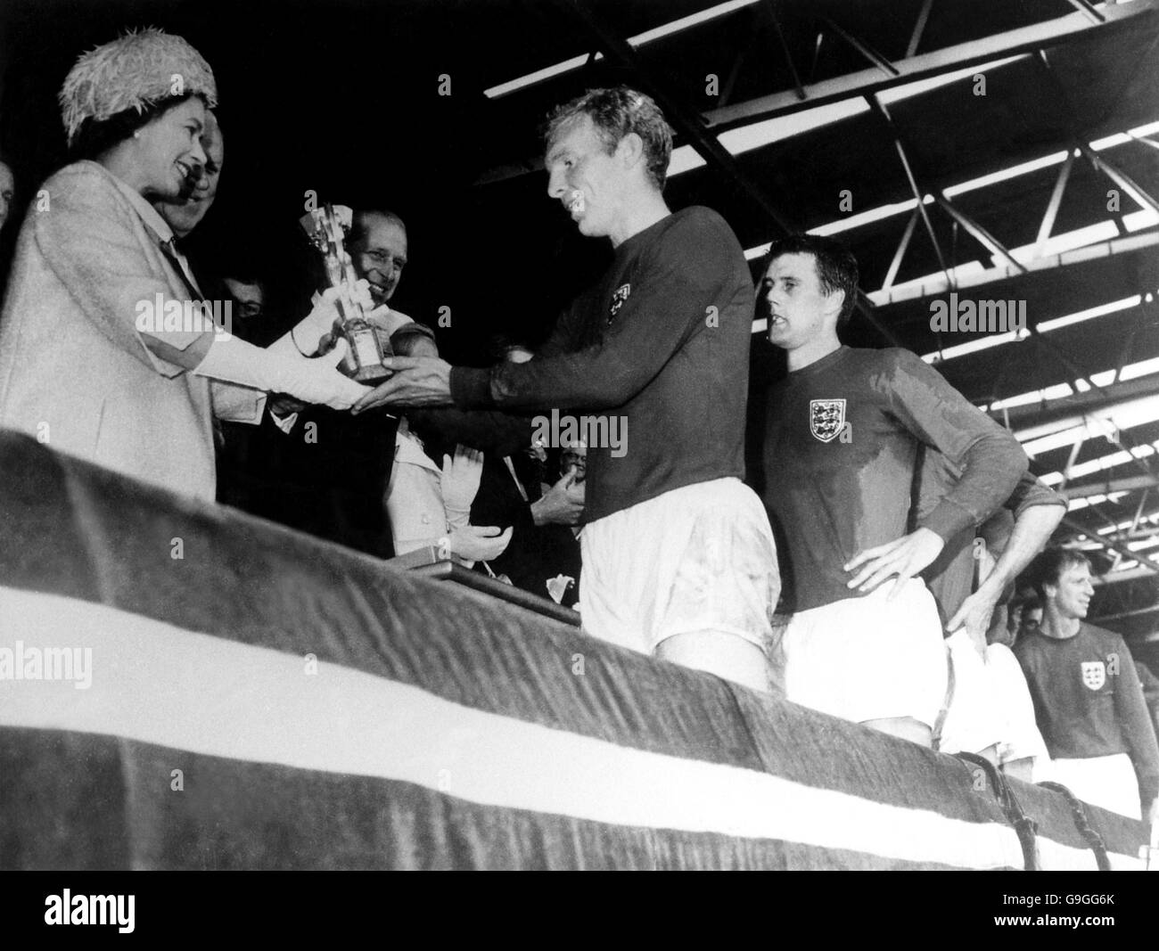 Le capitaine d'Angleterre Bobby Moore reçoit la coupe du monde Trophée de sa Majesté la Reine comme Geoff Hurst regarde on en est émerveillé Banque D'Images