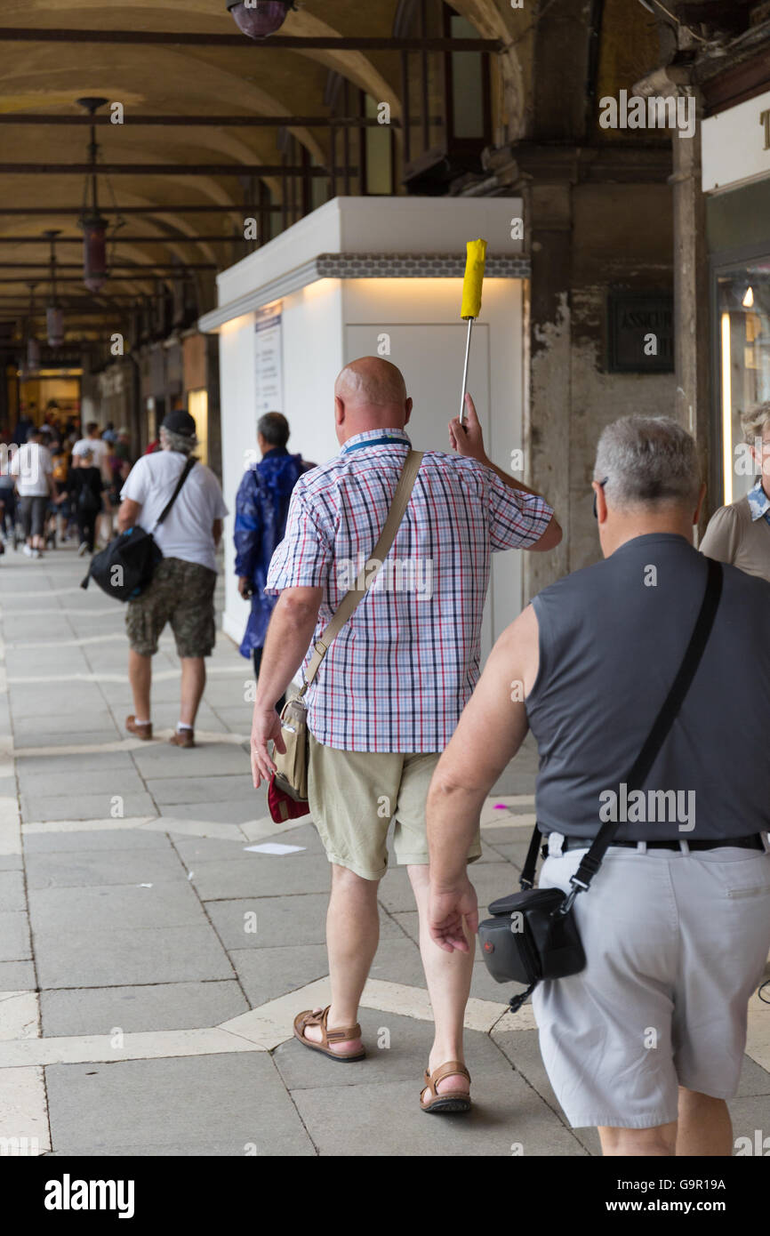 Un guide touristique à Venise, en marchant à travers la place St Marc holding up un parapluie Banque D'Images