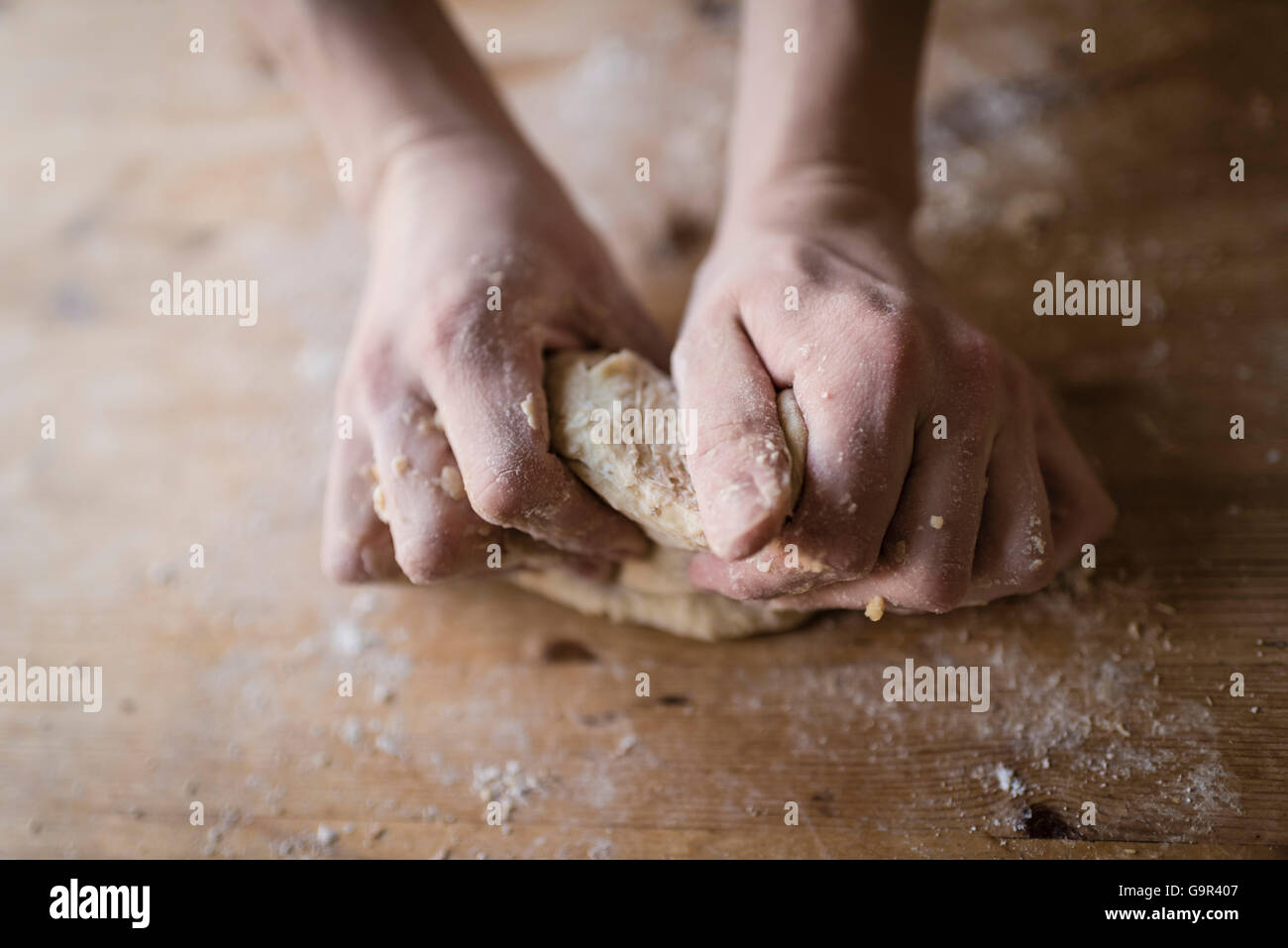 Close-up de deux mains fortes d'un baker que sont la pâte à pétrir manuellement sur une table de cuisine en bois, Banque D'Images