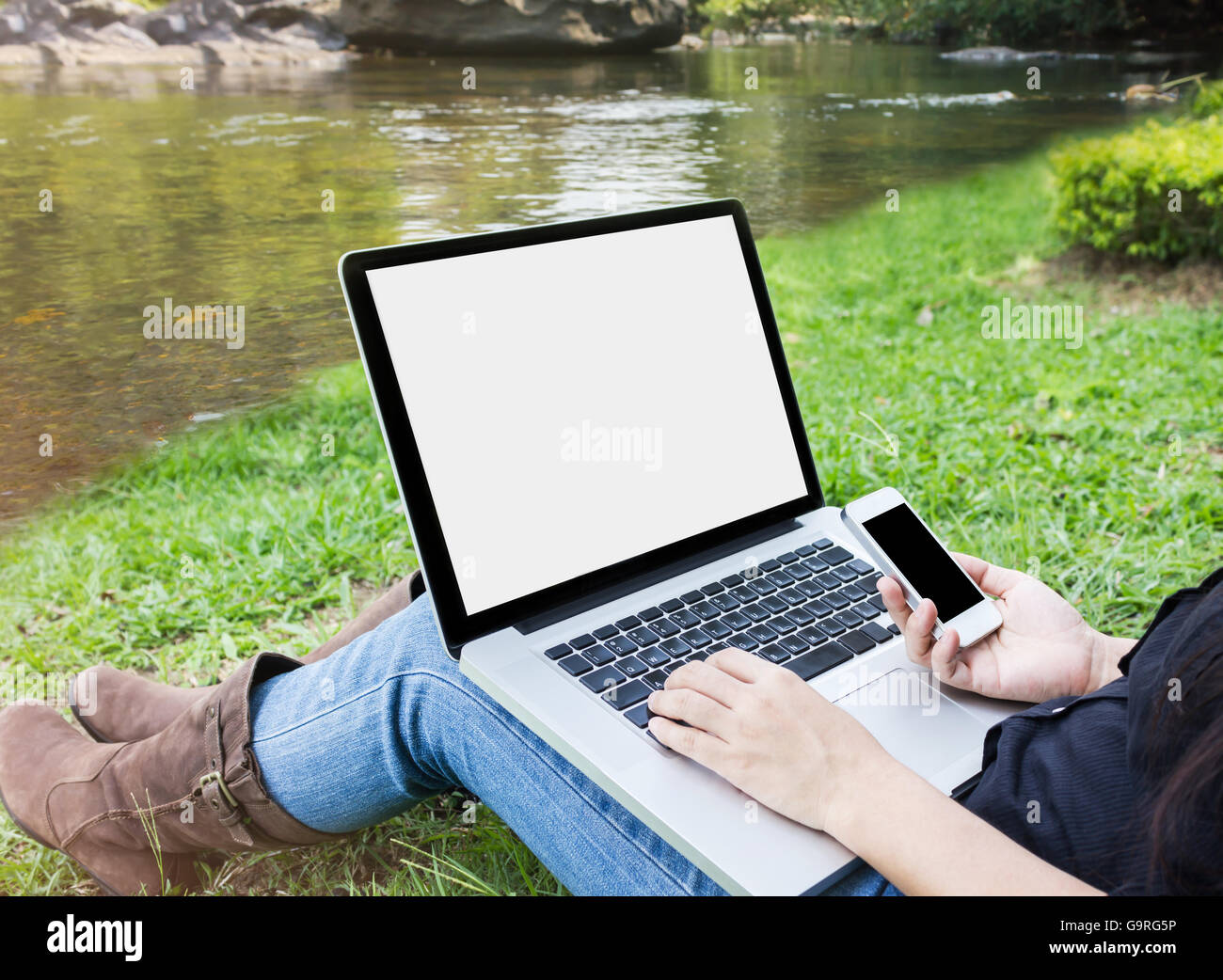 Ordinateur portable avec écran vide girl sitting on grass field at Riverside, fille ou femme avec le smartphone dans la main internet surf en rel Banque D'Images