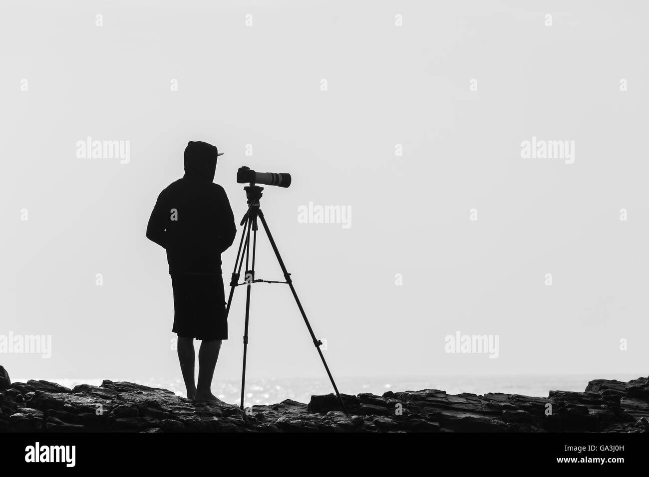 Trépied photo avec photographe non identifié qui se profile sur les rochers plage vintage sépia Noir et blanc. Banque D'Images