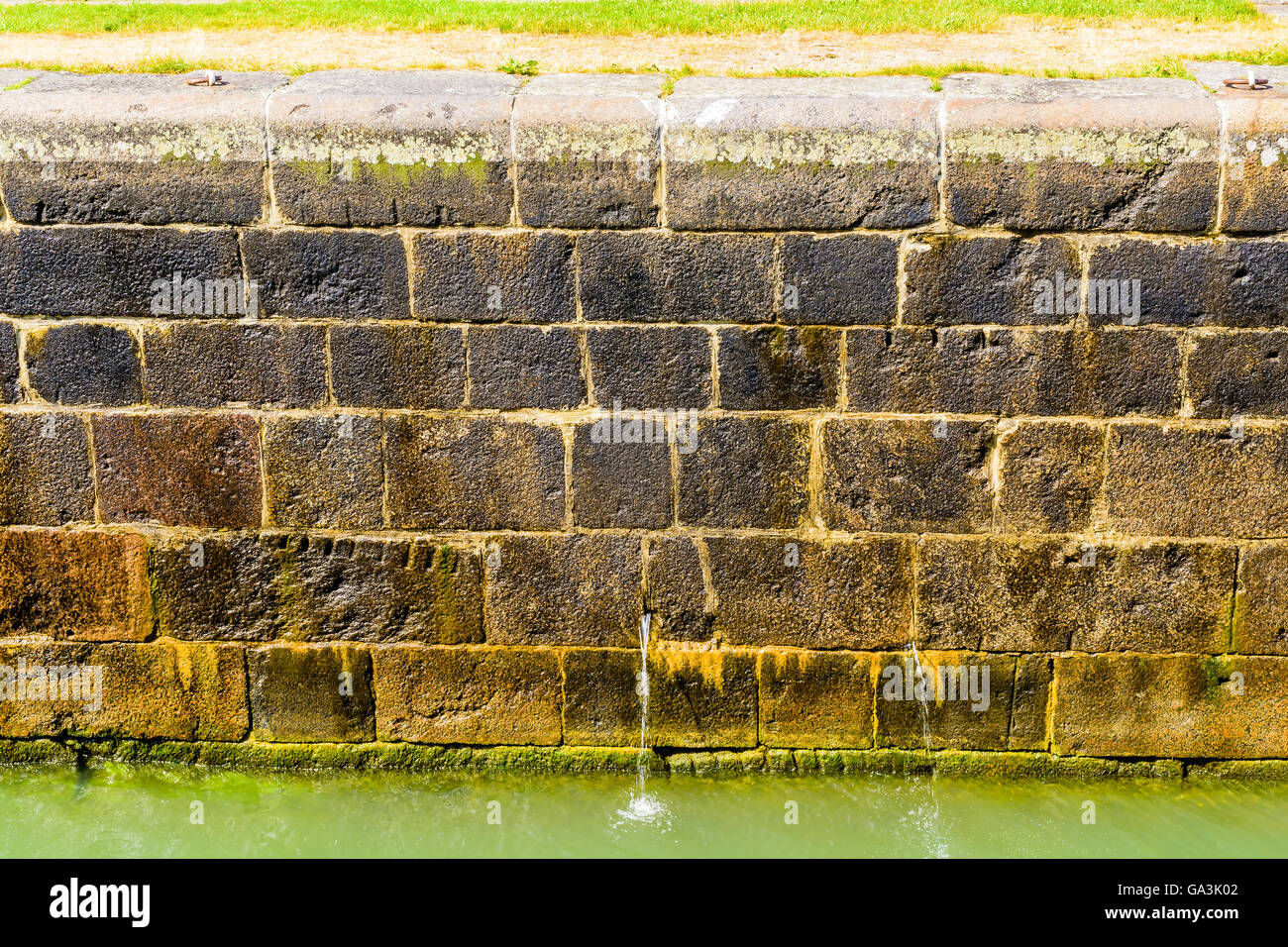 Blocs de pierre humide à un mur du canal avec de l'eau qui s'écoule d'un petit trou dans le mur. Banque D'Images